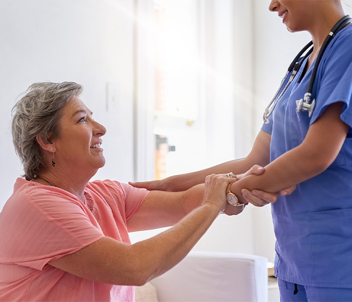 A caregiver in blue scrubs helping an elderly woman in therapy.