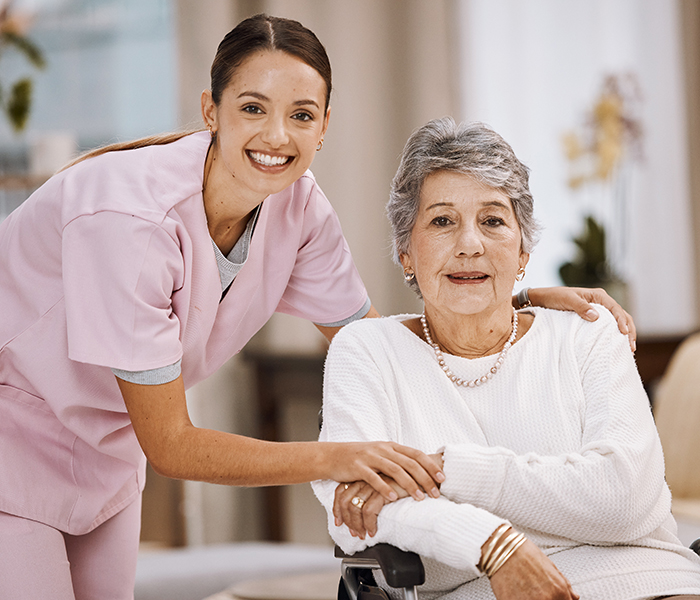 Caregiver assisting an elderly woman in a wheelchair indoors.