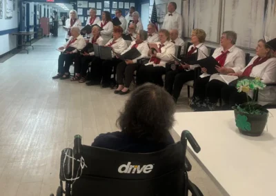 Residents choir performance in a care center hallway with seated audience member in foreground