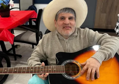Smiling male resident wearing a cowboy hat and casual clothing, playing an acoustic guitar
