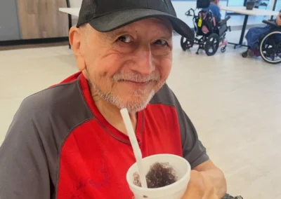 A smiling male resident wearing a black baseball cap holding a cup of shaved ice with a straw.