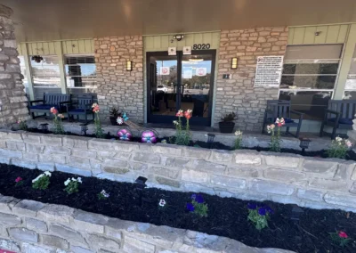 Front entrance with brick exterior, glass doors, flowering landscape beds, and potted plants